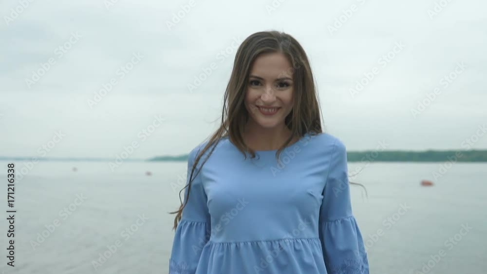 Young beautiful woman in a blue dresswalking on the water along the beach. She posing for the camera, looking very happy. Young beautiful woman in a blue dresswalking on the water along the beach. She posing for the camera, looking very happy.