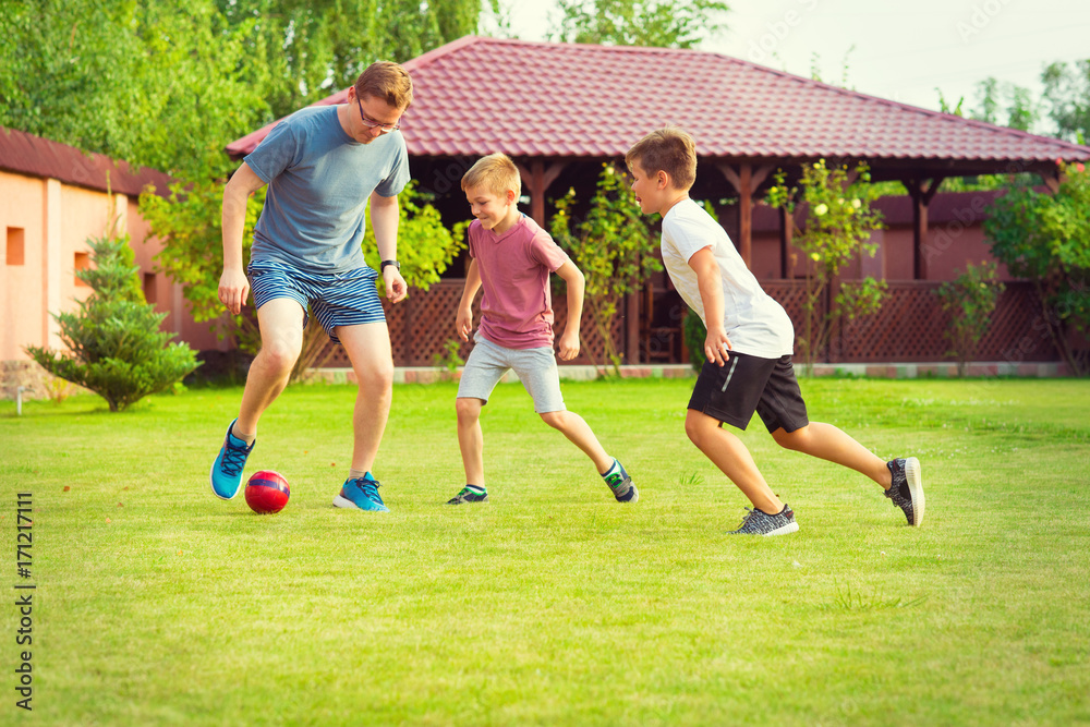 Two happy sons playing football with their father in garden near House Two happy sons playing football with their father in garden near House
