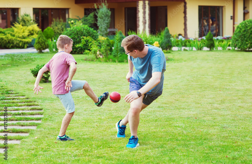 Two happy sons playing football with their father in garden near House Two happy sons playing football with their father in garden near House