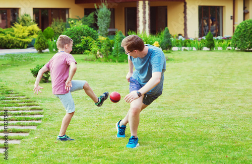 Two happy sons playing football with their father in garden near House