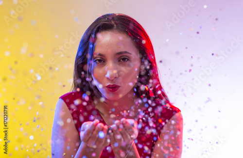 Beautiful girl on party background blowing confetti