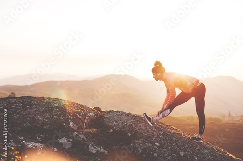 Athletic girl doing stretching after a good run in the mountains at sunset. Sport tight clothes.