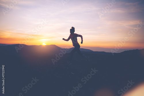 Silhouette of athletic girl finishes workout in the mountains at sunset. Sport tight clothes. Intentional motion blur.