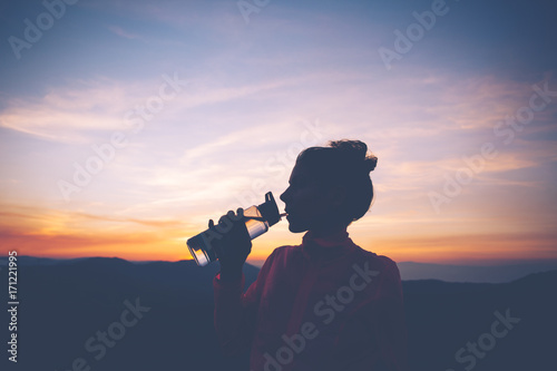 Silhouette of ahletic woman drinks water while relaxing during training in the mountains at sunset. Sport tight clothes. photo