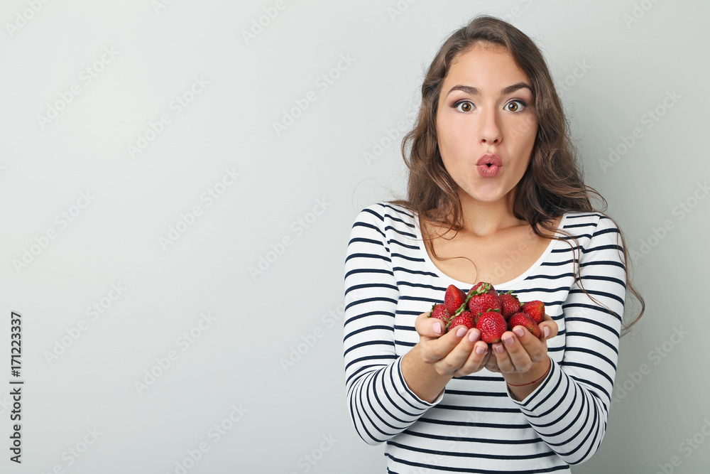 Portrait of young woman with strawberries on grey background Portrait of young woman with strawberries on grey background