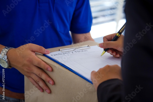Close up Delivery man in blue uniform holding package while woman is signing  receiving documents.