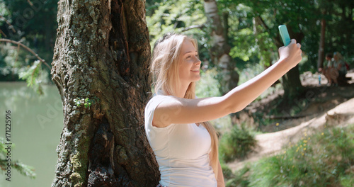 Young woman taking a selfie by a smartphone in a forest. Beautiful caucasian girl spending time in a moutain woods.