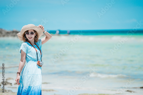 Young Asian woman wearing Hawaiian with hat and sunglasses is happy when they go to the beach for a holiday.