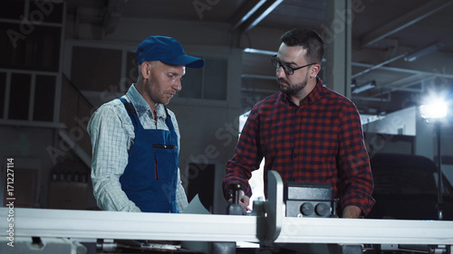 Adult men standing in joinery shop and coworking with blueprints.