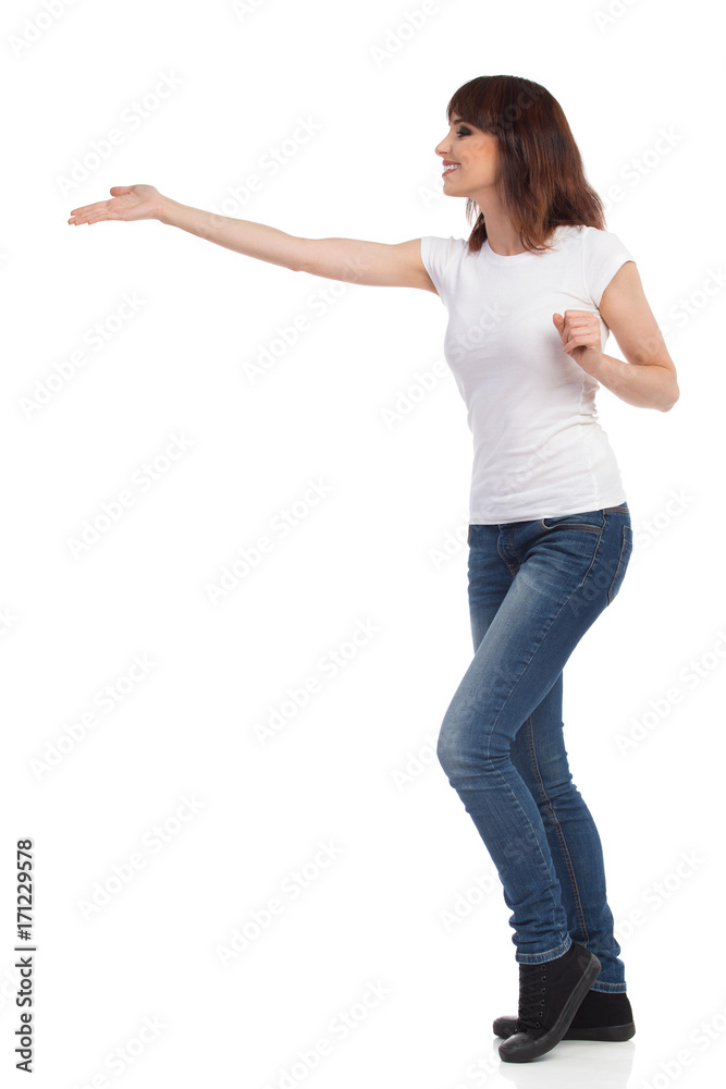 Smiling Woman In Jeans And White T-shirt Is Presenting. Side View. Smiling Woman In Jeans And White T-shirt Is Presenting. Side View.