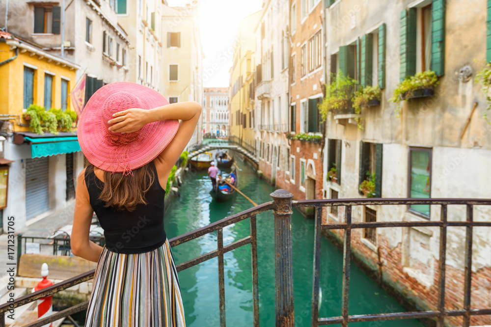 Obraz premium Kobieta z czerwonymi słońce kapeluszu spojrzeniami na kanale z gondolą w Wenecja, Włochy