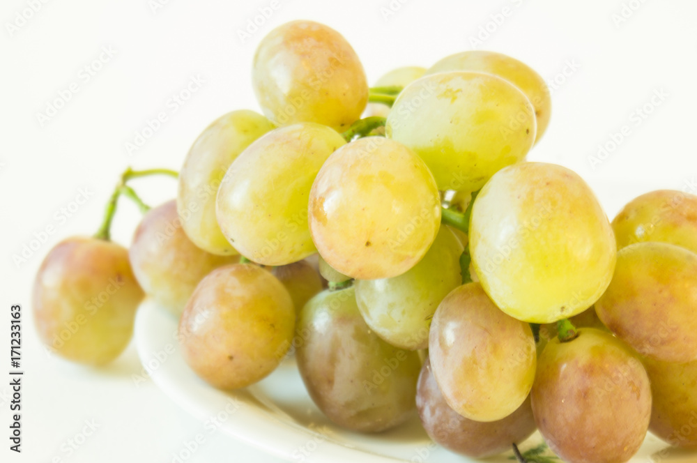 Виноград. Гроздь розового винограда на белом блюдце и белом фоне