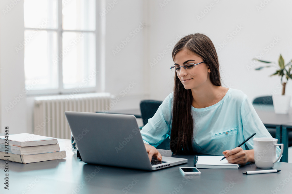 Portrait of smiling businesswoman with laptop writes on a document at her office Portrait of smiling businesswoman with laptop writes on a document at her office