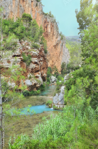 Hiking trail of Chillapajaros, in Montanejos (Castellon - Spain). View of Mijares river. People doing rafting at the background. Green environment. Colorful landscape. Rocky cliffs