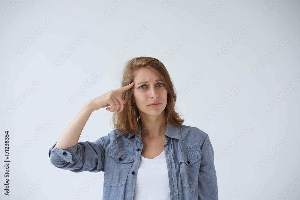Headshot of emotional annoyed young Caucasian woman having indignant expression on her face, twisting index finger at her temple as if saying: Are you crazy? Stop talking nonsense. Body language Headshot of emotional annoyed young Caucasian woman having indignant expression on her face, twisting index finger at her temple as if saying: Are you crazy? Stop talking nonsense. Body language