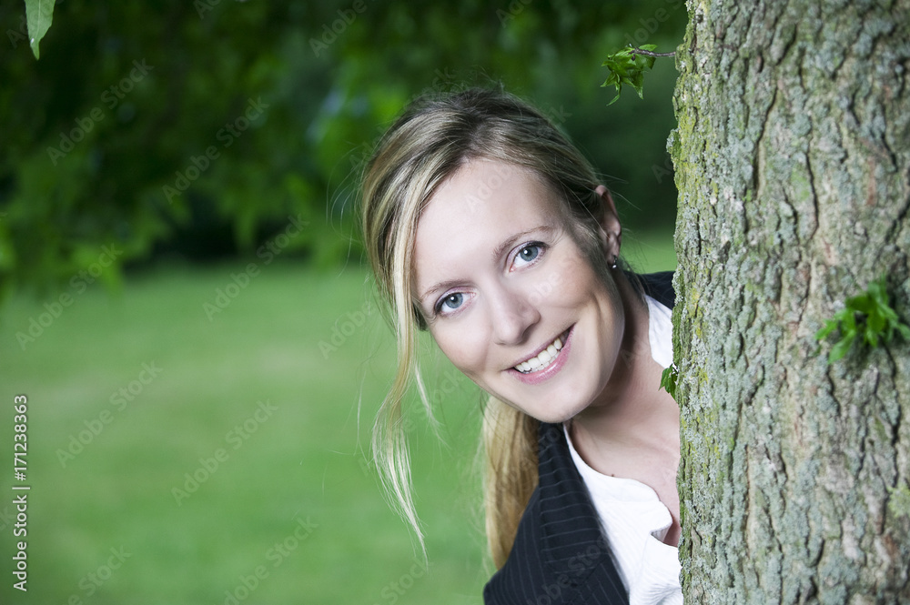 young blond woman looking from behind a tree young blond woman looking from behind a tree