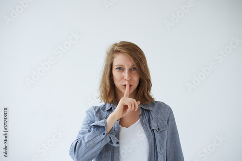 Silence, secret, conspiracy, confidential information and taboo concept. Portrait of mysterious young European woman dressed casually saying shh, holding finger on her lips, asking to keep silent