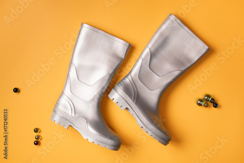 Autumn creative composition: From above view of stylish silver gumboots and small glass balls on orange background. Top view. Flat lay.