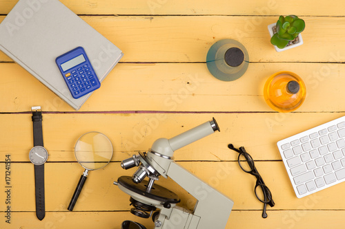 Education and science concept - microscope, book, magnifying glass, calculator, watch, blank clipboard, computer keyboard, eyeglasses and chemical liquids