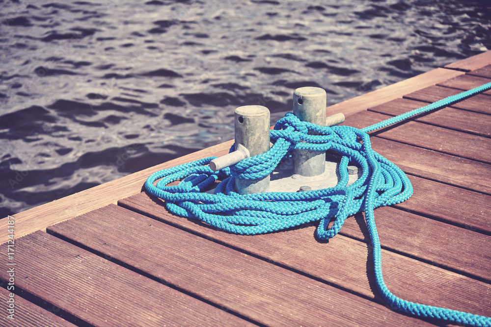 Obraz premium Vintage toned picture of a cleat with blue rope on a wooden pier, shallow depth of field.