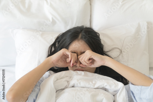 Beautiful Asian young woman hands rubbing her eyes. Asian long hair girl lying on white bed.