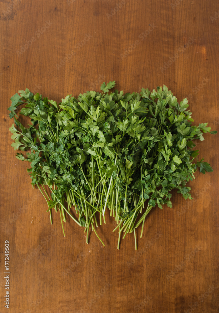 Bunch of fresh, wet garden parsley stems with little imperfections on wooden background Bunch of fresh, wet garden parsley stems with little imperfections on wooden background