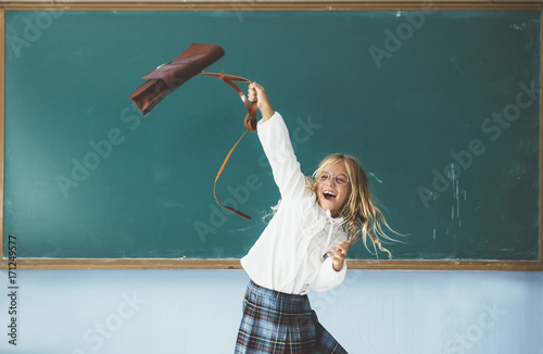 Happy girl throwing backpack in the classroom photo