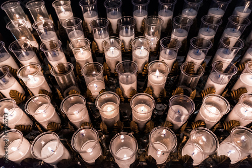 Fotografie Closeup pattern of many white religious votive candles with yellow flame in chur