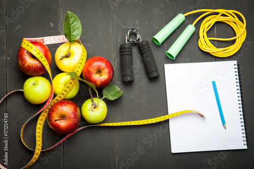 A green apple is wrapped in a centimeter against the background of a heavy dumbbell on a wooden floor