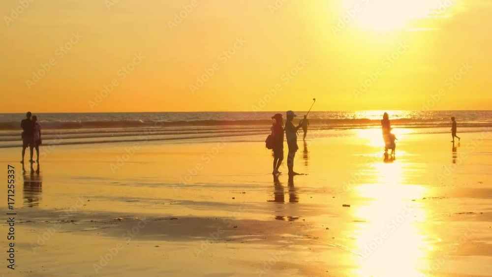 KUTA, BALI, INDONESIA - MAY 1st 2017: Tourists exploring crowded Kuta Beach in gorgeous Bali at golden light sunset. Friends taking selfies using selfie-stick, kids running, people enjoying vacations KUTA, BALI, INDONESIA - MAY 1st 2017: Tourists exploring crowded Kuta Beach in gorgeous Bali at golden light sunset. Friends taking selfies using selfie-stick, kids running, people enjoying vacations