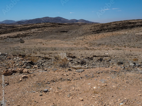 Rock mountain dried dusty landscape ground of Namib desert with splitting shale, other stone and desert plant