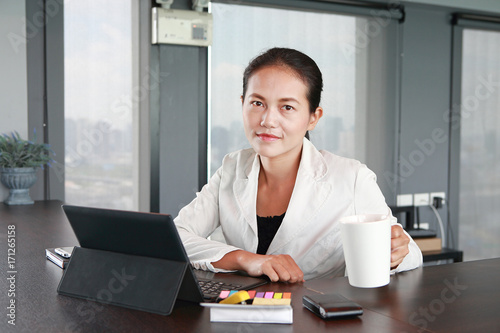 Young businesswoman sitting at the table on workplace in office with laptop computer drinking a coffee.