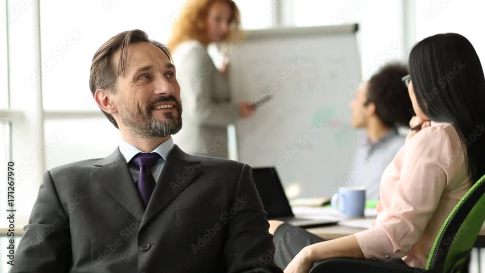 Smiling businessman sitting in the office with his back to coworkers. Happy director on meeting of team of coworkers. Smiling businessman sitting in the office with his back to coworkers. Happy director on meeting of team of coworkers.