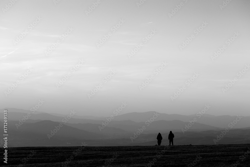 A couple on top of a mountain at near sunset, with soft tones and distant hills and mountains