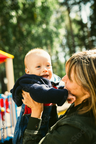 Portrait of mother who hug her joyful baby boy. Outdoors healthy child activity, active lifestyle and having fun on family summer vacation with son at the playground.