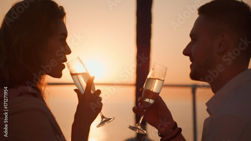 Beautiful loving couple drinking champagne with smile on yacht looking at sunrise together slow motion