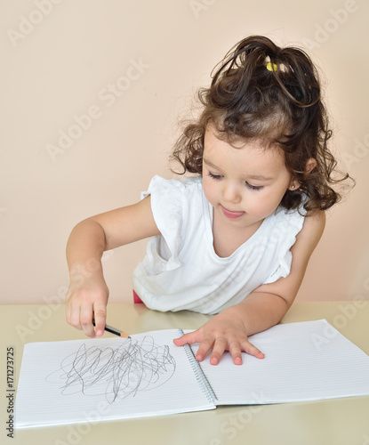 Cute young girl drawing with a pencil in the notebook
