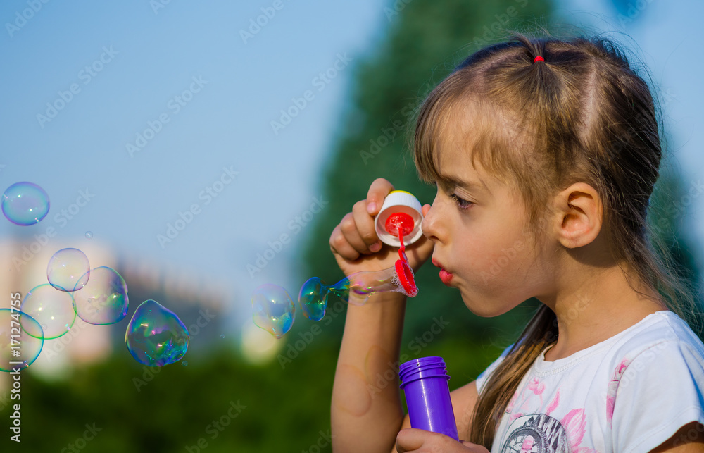 Close-up a girl of six-years blowing soap-bubble outdoor in the park.