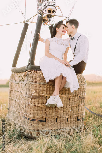 The composition of the airballon placed in the sunny field. The newlyweds are sitting head-to-head in the basket. photo