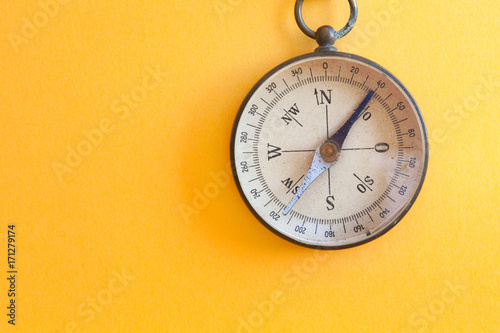 Vintage compass retro style travel instrument used for navigation orientation geographic cardinal directions north, south, east, and west. Yellow paper textured background, copy space photo