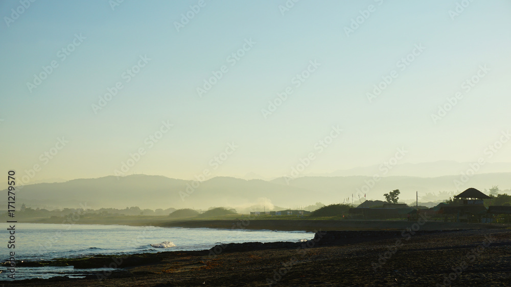 Foggy beach shore and coast sunrise with mountain silhouette