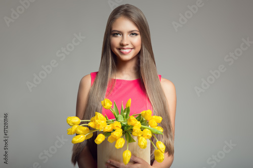 Young happy woman holding basket with yellow tulips. Gray background.