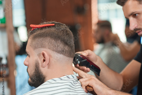 Cropped close up of a professional barber working at his barbershop giving a haircut to his male client.