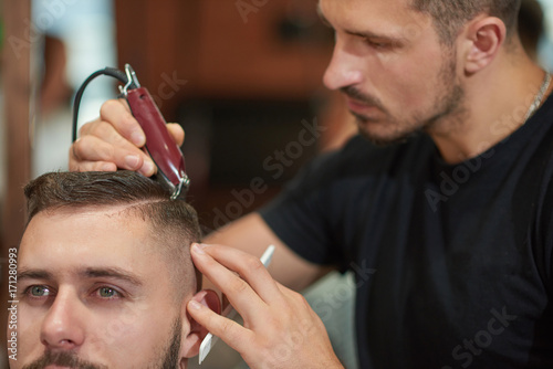 Cropped shot of a professional barber working using a clipper styling hair of his client. 