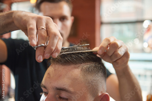 Close up shot of a barber using scissors cutting hair of his male customer. 