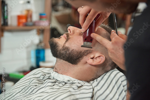 Close up shot of a young bearded man getting his beard shaped and trimmed at the barbershop. 