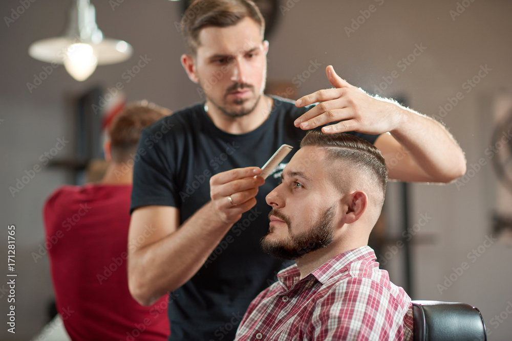 Portrait of a young barber styling hair of his bearded client. Portrait of a young barber styling hair of his bearded client.