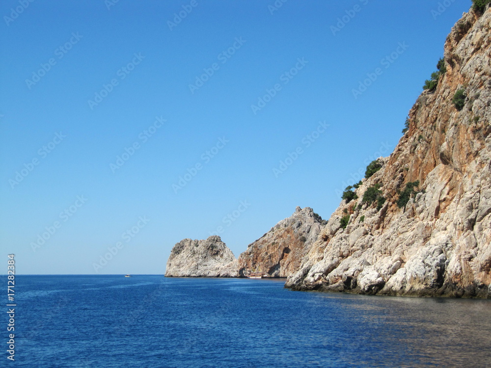 The blue sea with beautiful brown rocks with the ruins of an old fortress. Turkey, Alanya
