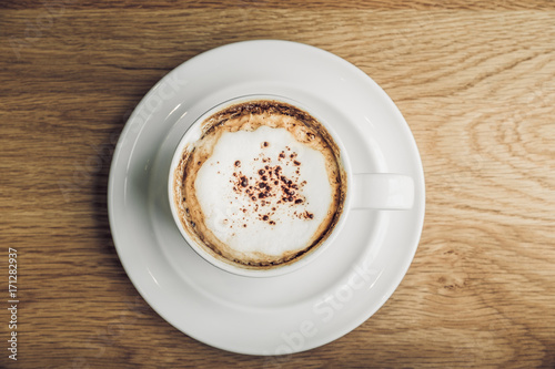 Top view of hot cappuccino in white coffee cup on brown wood table near window in morning vintage filtered 