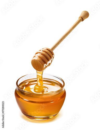 Glass jar and honey dripping from dipper isolated